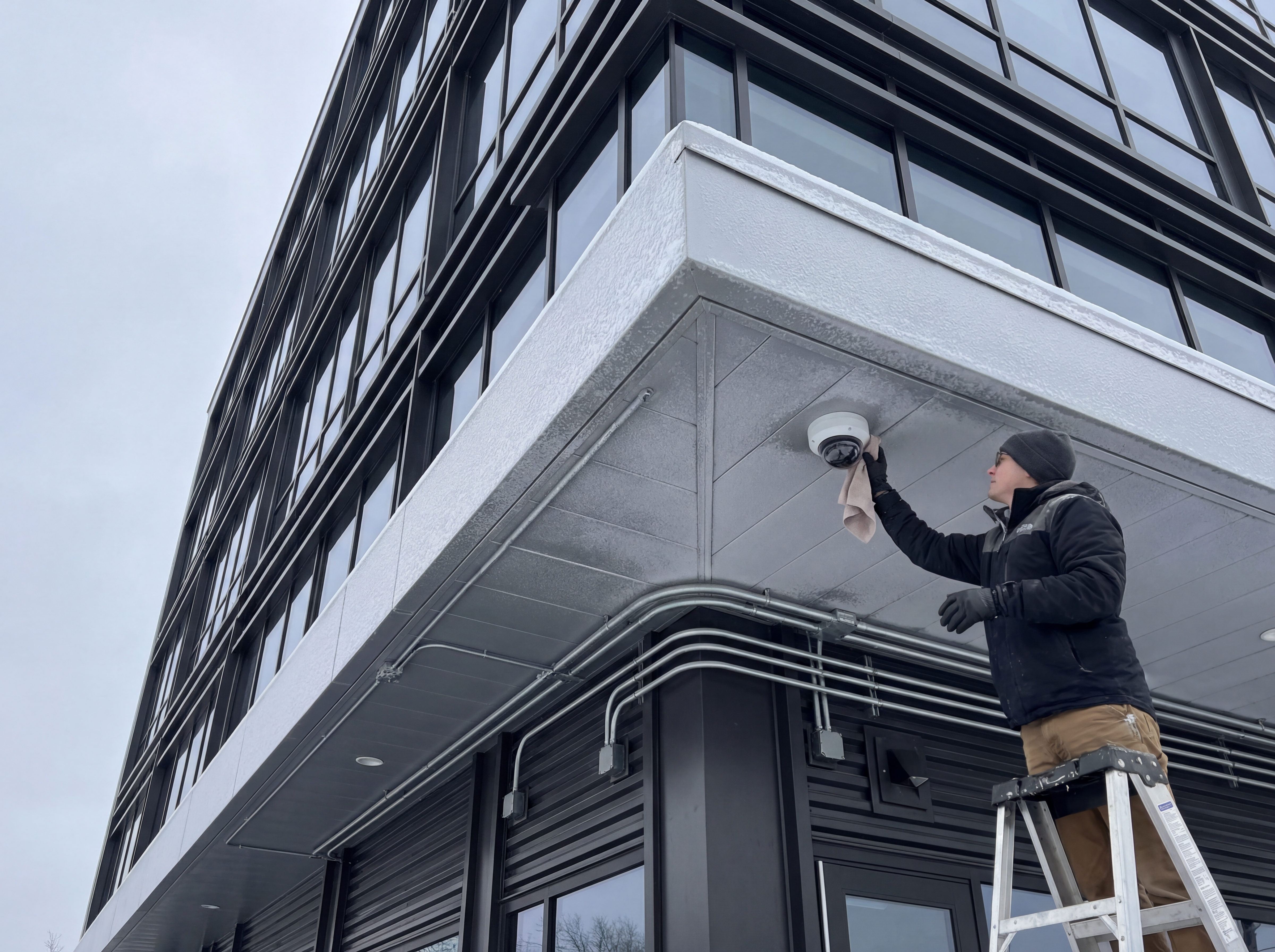 Homeowner wiping a security camera under a snowy roofline